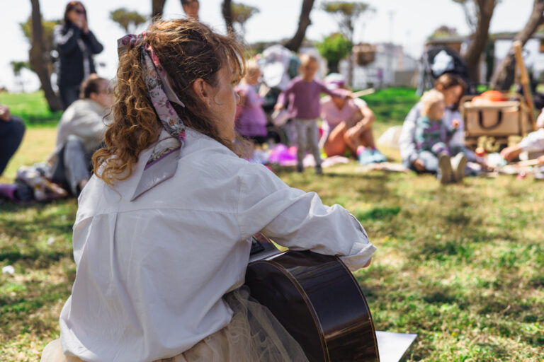person-playing-guitar-outdoors-while-sitting-grass-sunny-day-with-tambourine-nearby (1)